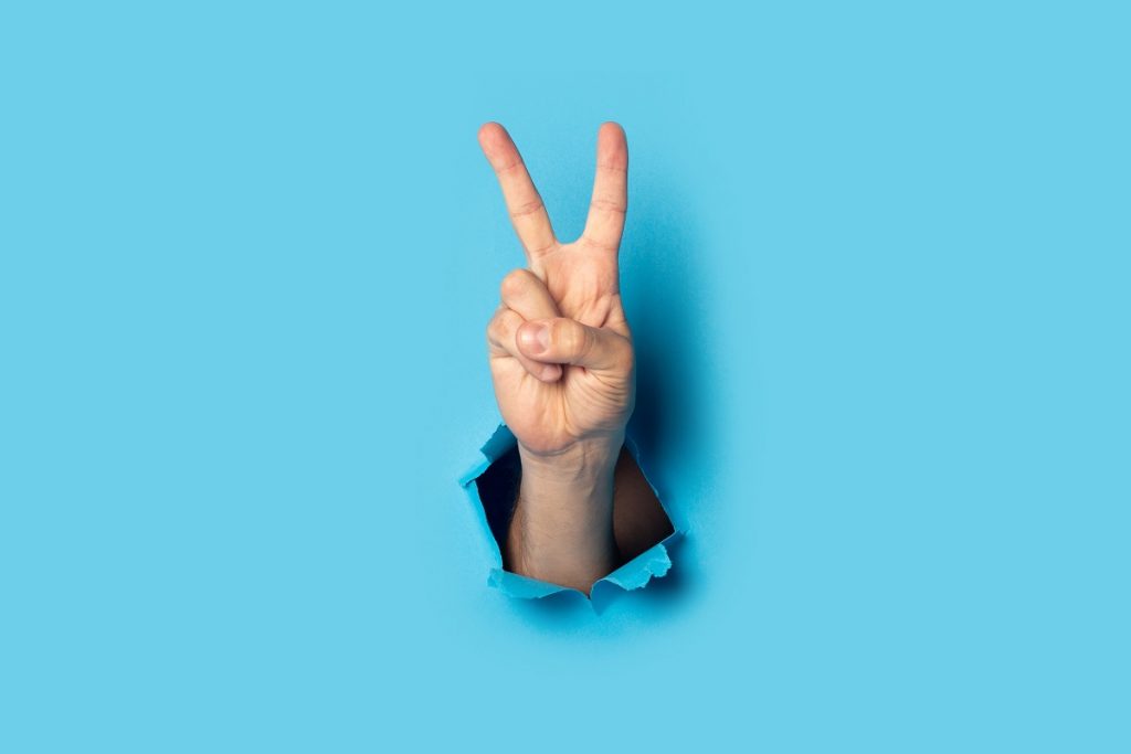 Male hand makes a two fingers up greeting gesture on a blue background. Banner.