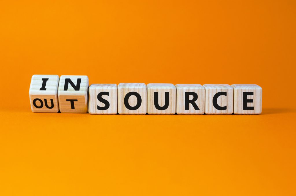Outsource or insource symbol. Fliped wooden cubes and changed the word 'outsource' to 'insource'. Beautiful orange background, copy space. Business and outsource or insource concept.